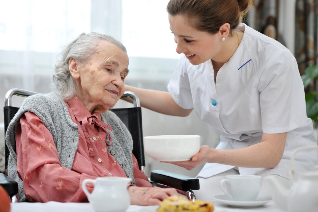 A nurse is serving food to an elderly woman.